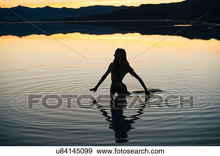 Stock Photo - "Silhouetted young woman wading in lake at sunset, Bonneville Salt Flats, Utah, USA". Fotosearch