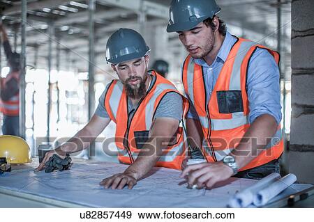 Site foreman and builder looking at blueprint in construction site View Large Photo Image Stock Photo - Site foreman and builder looking at blueprint in construction site. Fotosearch