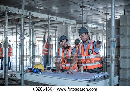 Stock Photo - Site foreman and builder pointing from blueprint in construction site. Fotosearch