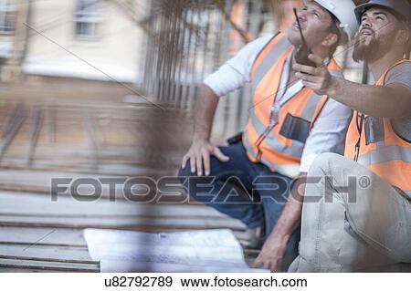 Stock Photo - Site manager and builder pointing up from blueprint on construction site. Fotosearch