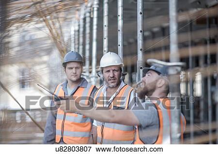 Stock Photo - Site manager and builders pointing to steel rods on construction site. Fotosearch