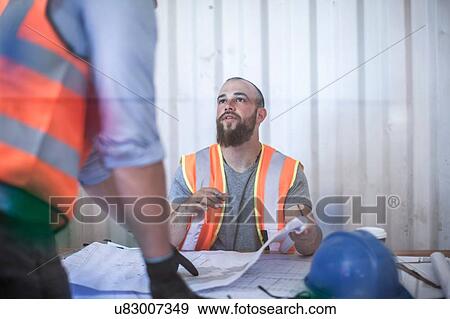 Site manager sitting at desk explaining blueprint to worker in portable cabin View Large Photo Image Stock Photo - Site manager sitting at desk explaining blueprint to worker in portable cabin. Fotosearch