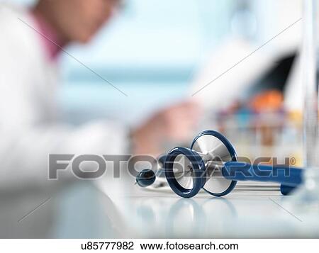 Stock Image - Stethoscope on desk, doctor in background. Fotosearch