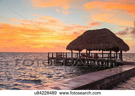 Stock Photo - "Stilted waterfront pier and thatched roof at sunset, St. Georges Caye, Belize, Central America". Fotosearch