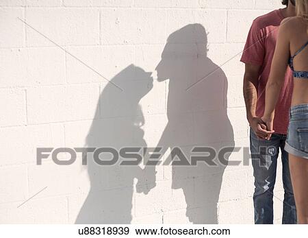 Stock Photo - Sunlit shadow of young couple holding hands and kissing. Fotosearch