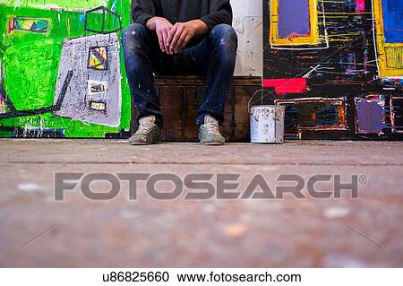 Stock Image - Surface view of male artist sitting between canvases. Fotosearch