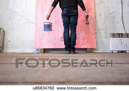 Stock Image - Surface view of male artist standing in front of canvas. Fotosearch