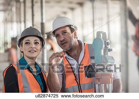 Stock Photography - Surveyor explaining to female builder on construction site. Fotosearch