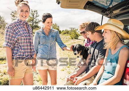 Stock Image - Teenage girl, adult friends and dog sitting on car boot, Bridger, Montana, USA. Fotosearch