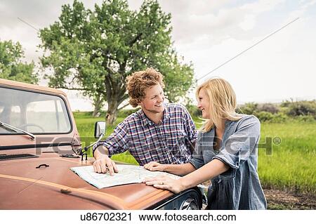 Stock Image - Teenage girl and boyfriend reading map on jeep hood. Fotosearch