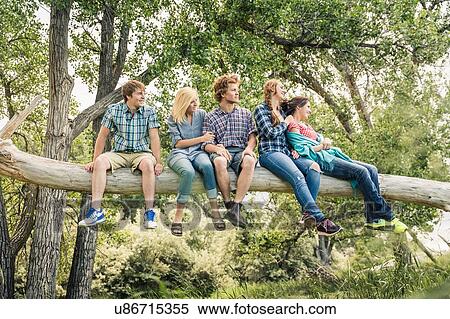 Stock Photography - Teenage girl and young adult friends looking out from fallen tree. Fotosearch