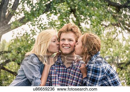 Stock Photograph - Teenage girl and young woman kissing happy young man on cheek. Fotosearch