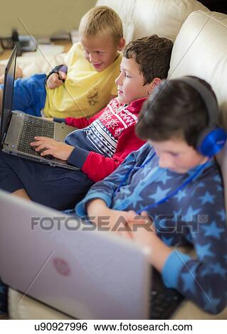 Stock Photograph - Three boys using laptops sitting on sofa. Fotosearch