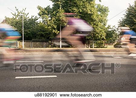 Stock Image - Three cyclists speeding on urban road in racing cycle race. Fotosearch