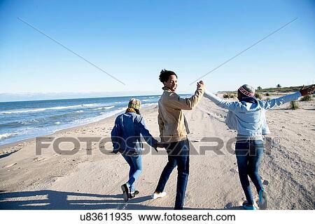 "Three friends walking along beach, holding hands, rear view" View Large Photo Image Stock Photography - "Three friends walking along beach, holding hands, rear view". Fotosearch