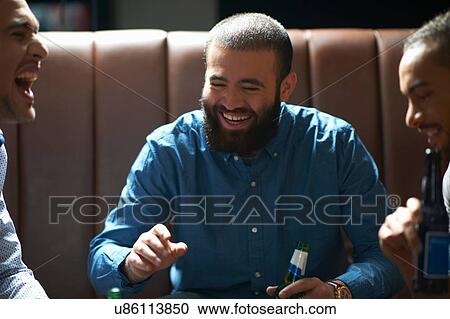 Stock Image - Three male friends chatting and laughing in traditional UK pub. Fotosearch