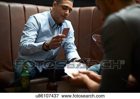 Stock Photo - Three male friends playing card game in traditional UK pub. Fotosearch