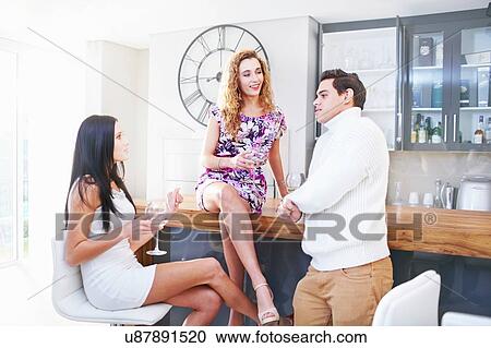 Three young adult friends drinking white wine in kitchen View Large Photo Image Stock Image - Three young adult friends drinking white wine in kitchen. Fotosearch