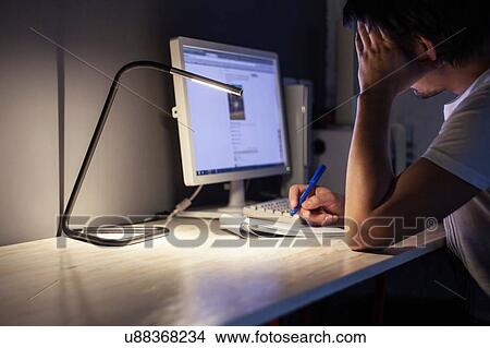 Picture - Tired man using desktop computer and making notes. Fotosearch