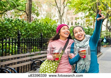Stock Photo - Twins walking with coffee and pointing up in park. Fotosearch