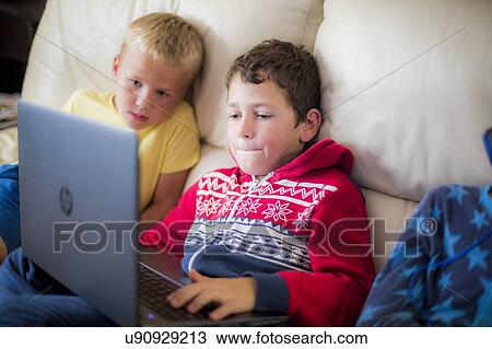 Stock Image - Two boys using a laptop sitting on sofa. Fotosearch