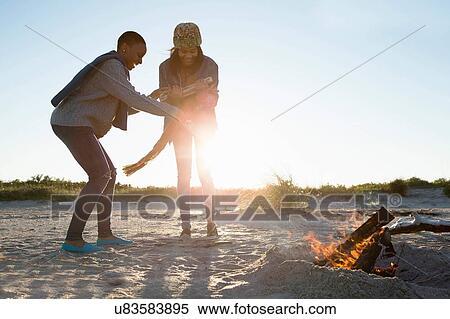 Stock Photography - "Two friends on beach, holding wood for camp fire". Fotosearch