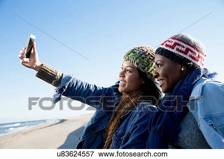 "Two friends sitting on beach, taking self portrait, using smartphone" View Large Photo Image Stock Photo - "Two friends sitting on beach, taking self portrait, using smartphone". Fotosearch