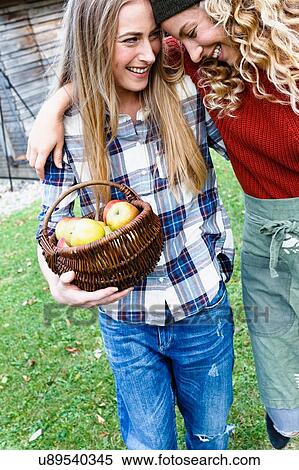 Two friends with arms round each other, one carrying basket of apples View Large Photo Image Stock Photography - Two friends with arms round each other, one carrying basket of apples. Fotosearch