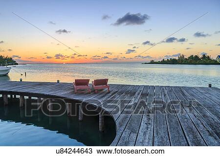 Stock Image - "Two sun loungers on waterfront boardwalk at sunset, St. Georges Caye, Belize, Central America". Fotosearch