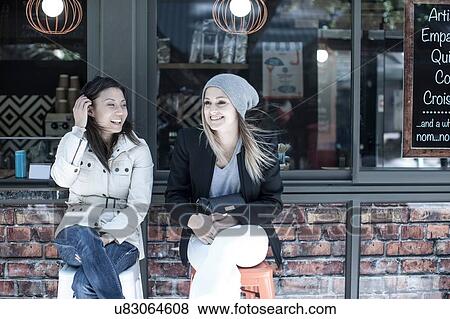 Stock Photo - Two women friends sitting outside city cafe. Fotosearch