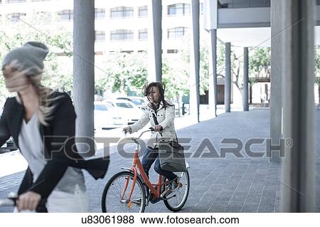 Two women friends with flyaway hair cycling in city View Large Photo Image Stock Photo - Two women friends with flyaway hair cycling in city. Fotosearch