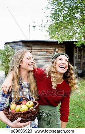 Stock Image - Two women in garden with basket of apples, laughing. Fotosearch