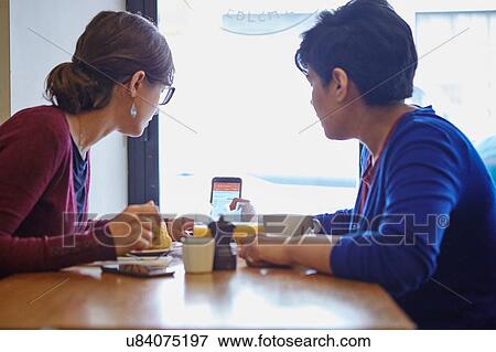Stock Photo - Two women reading smartphone text in restaurant. Fotosearch