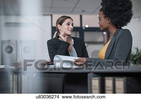 Picture - Two young businesswomen talking at office reception. Fotosearch