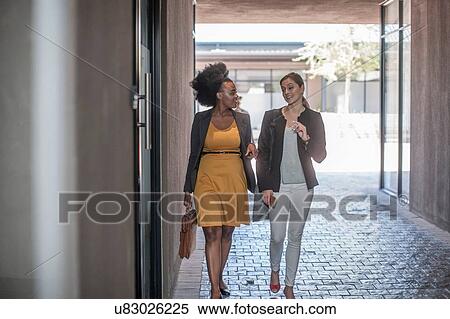 Stock Photography - Two young businesswomen walking and talking outside office. Fotosearch