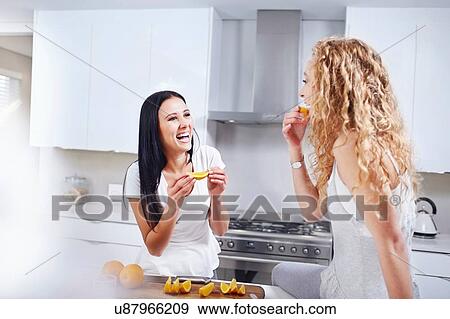 Two young female friends eating breakfast oranges at kitchen counter View Large Photo Image Stock Photo - Two young female friends eating breakfast oranges at kitchen counter. Fotosearch