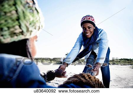 Stock Image - "Two young friends at beach, holding hands, smiling". Fotosearch
