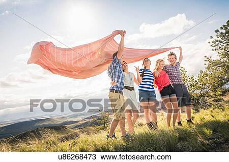 Stock Image - Two young men and female friends holding up blanket on windy hill, Bridger, Montana, USA. Fotosearch