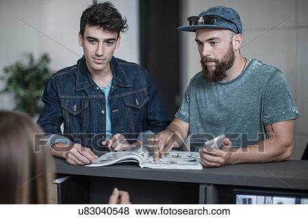 Two young men making query at office reception View Large Photo Image Stock Photo - Two young men making query at office reception. Fotosearch