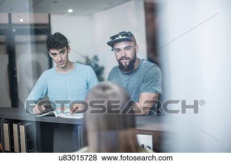 Stock Photo - Two young men querying receptionist in office. Fotosearch