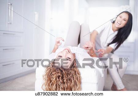 Stock Image - Two young women laughing and gossiping in bedroom. Fotosearch