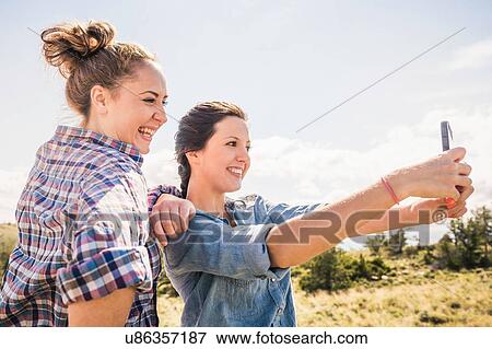 Stock Photo - Two young women taking selfie on smartphone, Bridger, Montana, USA. Fotosearch