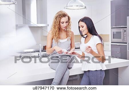 Two young women using digital tablet at kitchen counter View Large Photo Image Stock Image - Two young women using digital tablet at kitchen counter. Fotosearch