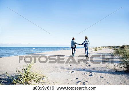 "Two young women, walking along beach, holding hands, rear view" View Large Photo Image Stock Photo - "Two young women, walking along beach, holding hands, rear view". Fotosearch