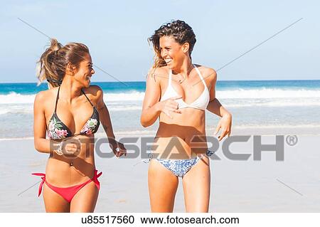 Stock Image - Two young women wearing bikinis running on beach, El Cotillo, Fuerteventura, Spain. Fotosearch
