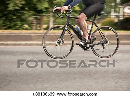 Stock Photo - Waist down view of racing cyclist speeding on urban road in racing cycle race. Fotosearch