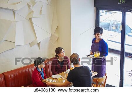 Stock Image - Waitress serving lunch in restaurant to family with son. Fotosearch