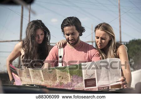 Stock Photo - Windscreen view of three young adult friends reading roadmap, Los Angeles, California, USA. Fotosearch