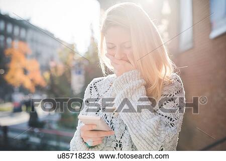 Stock Image - Woman amused with message on smartphone. Fotosearch
