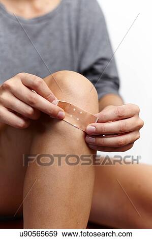 Stock Photo - Woman applying plaster on knee. Fotosearch